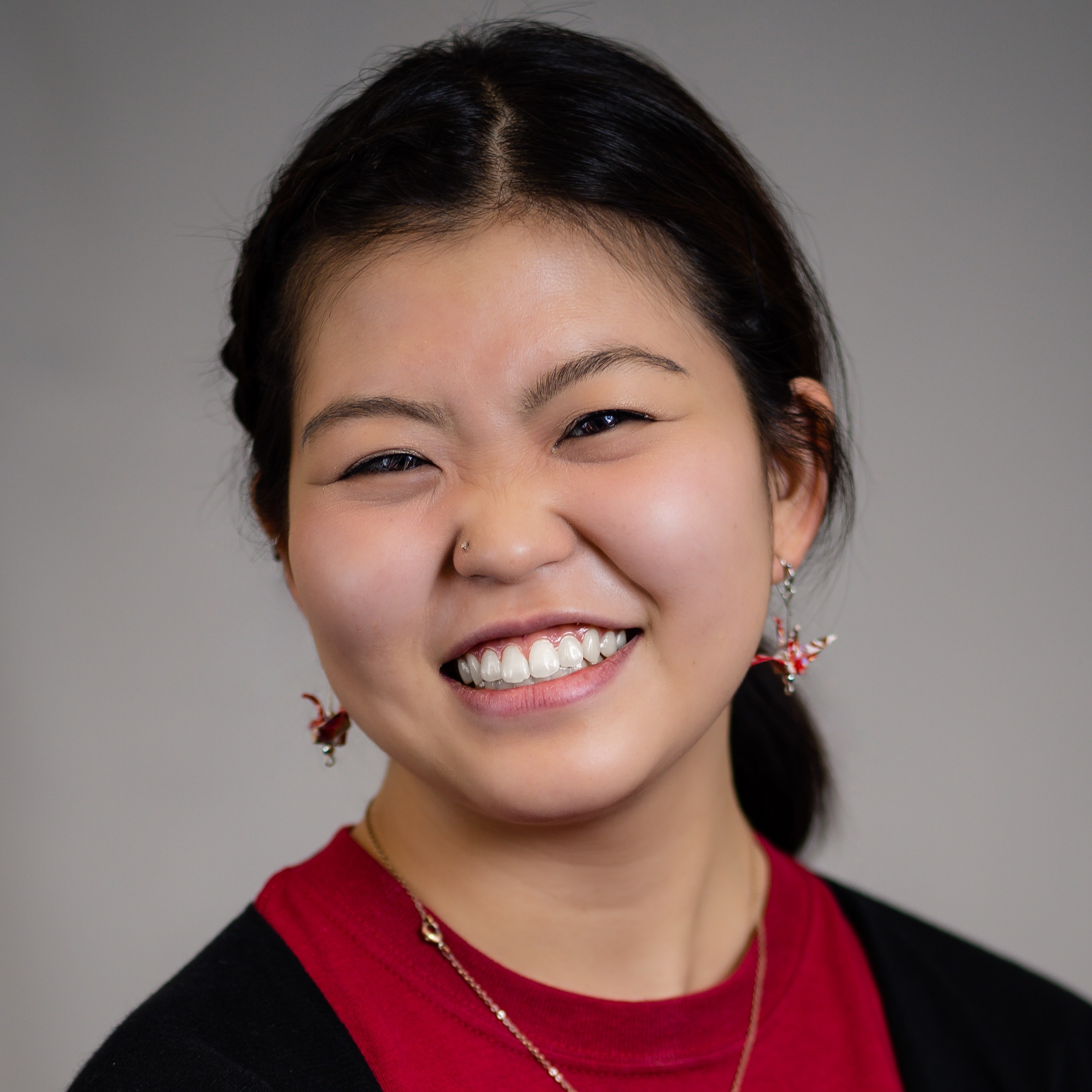 A smiling Asian person with a red shirt and paper crane earrings.
