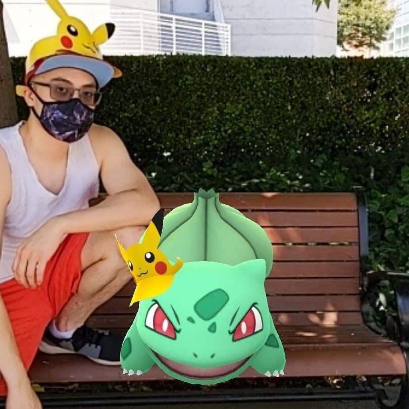 An Asian man posing on a bench with various animated Pokemon. 
